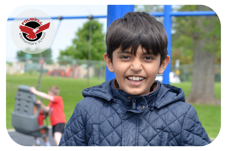 Folwell student smiling at the camera in front of playground outside.