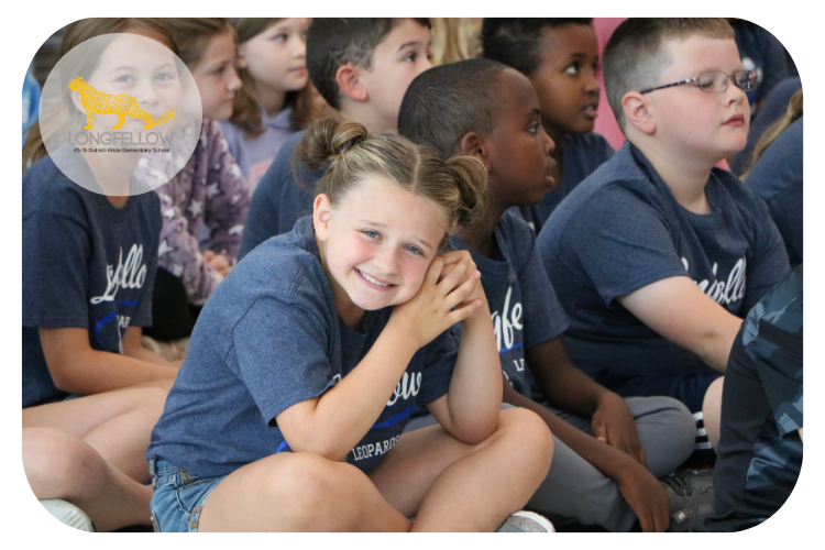 longfellow student smiling at the camera while assembled ini the cafeteria for a presentation.