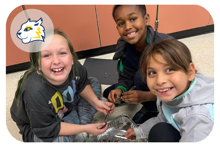 sunset terrace students smiling for a photo as they conduct a science experiment on the floor of the classroom.