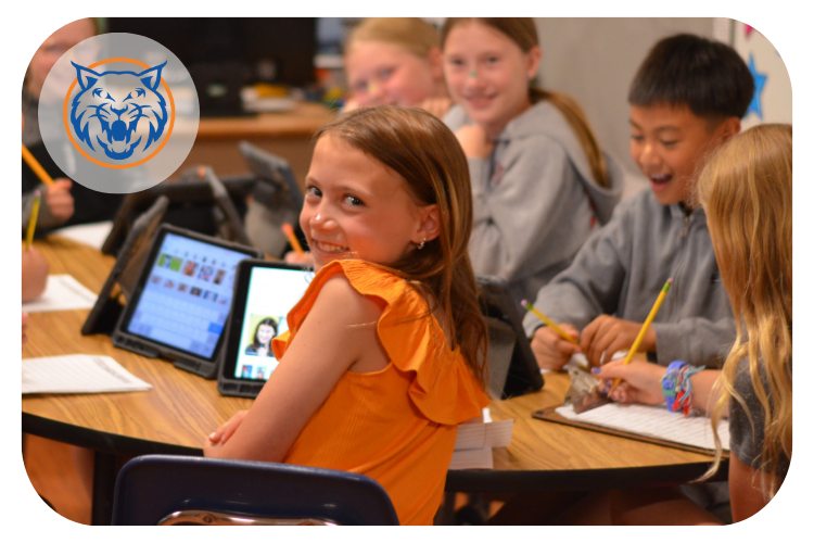 willow creek students gathered at a table to work through a classroom activity. One student look back at the camera and smiling.