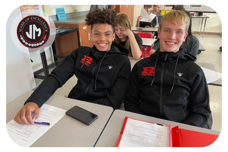 john marshall students in matching sweatshirts working on a math assignment and smiling at the camera.