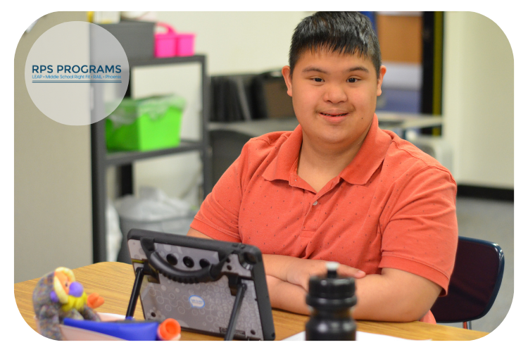 LEAP student working on his iPad and smiling at the camera.