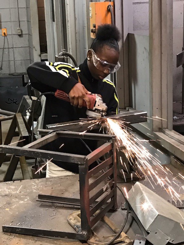 A student using an angle grinder on a steel bar
