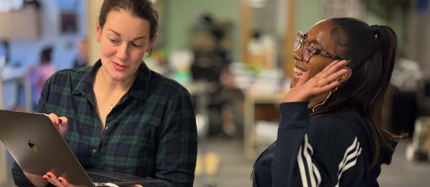 Two employees laughing and looking at a Macbook computer screen