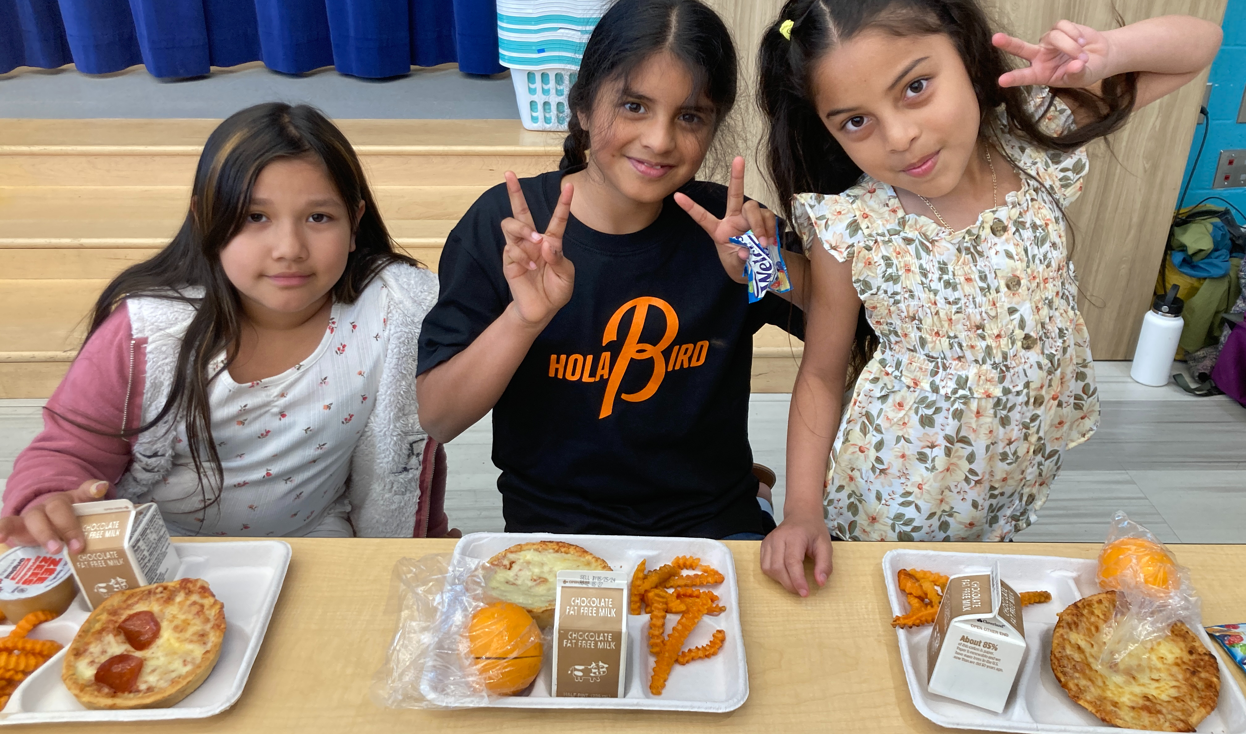Three students posing for the camera eating at a cafe table