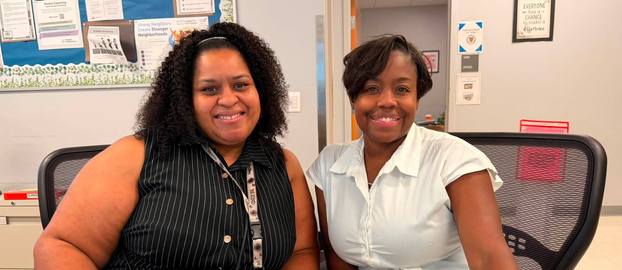 Two teachers sitting at their desk smiling at the camera