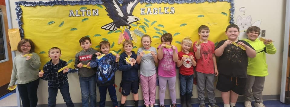 students stand in front of an eagle themed behavior bulletin board with feathers they earned
