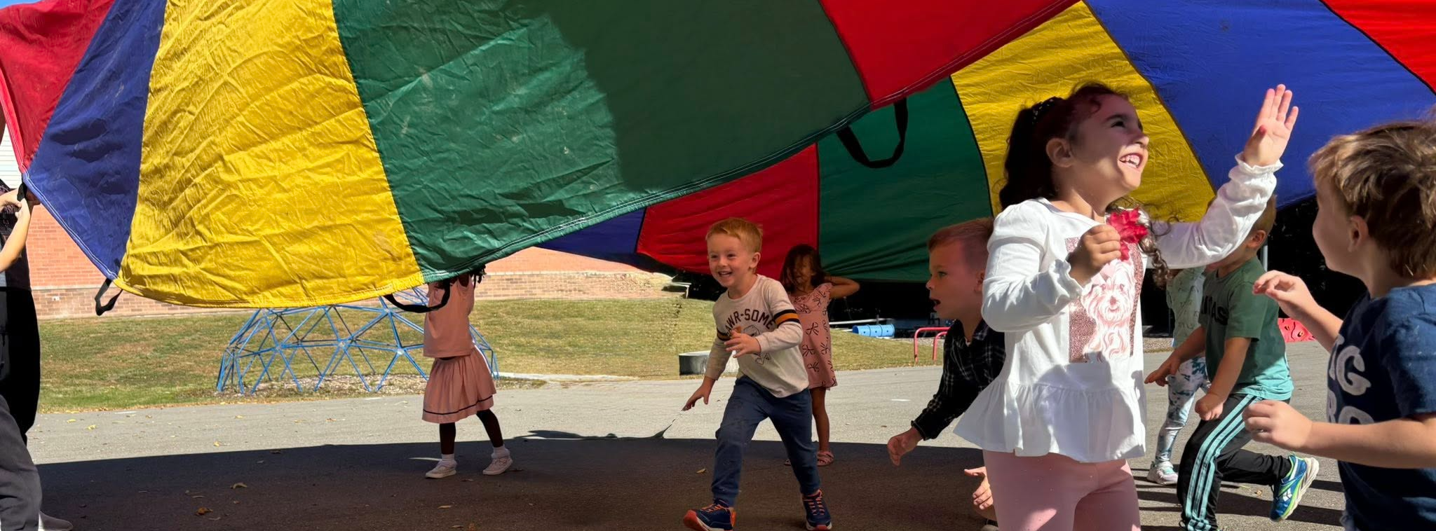 Pre-K students playing outside under a parachute