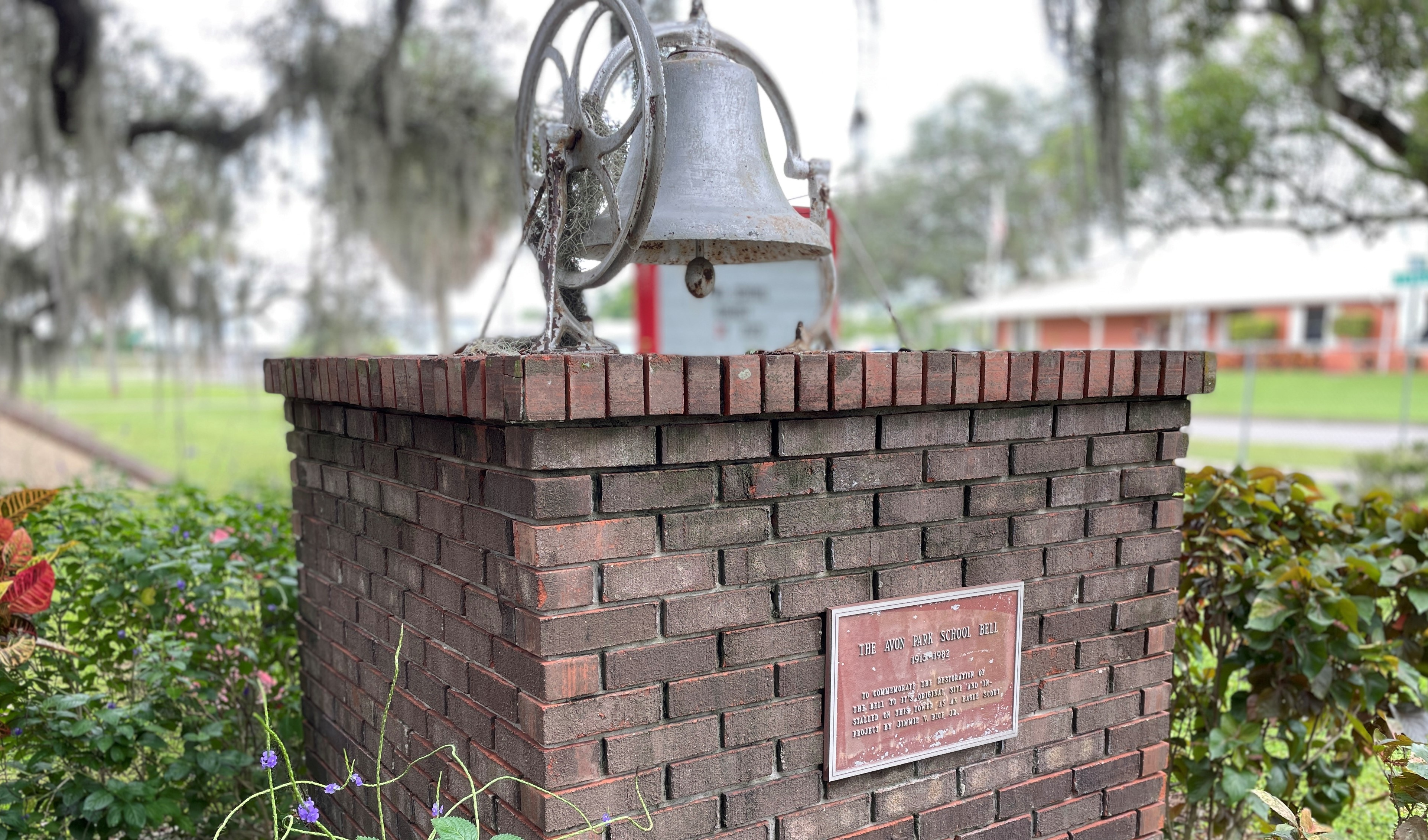 The APM bell that is in the front courtyard of the school.  The bell is a classic school bell that is mounted upon a large brick feature.  There is a plaque on the front indicating it was the original school bell before the current building was built.