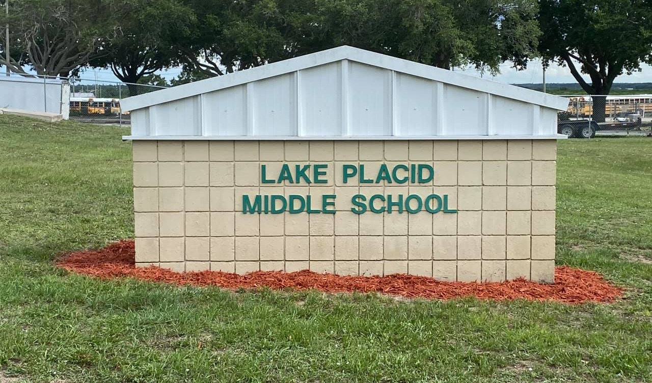 Lake Placid Middle School Sign in the front of the school with green lettering on beige block surrounded by mulch.