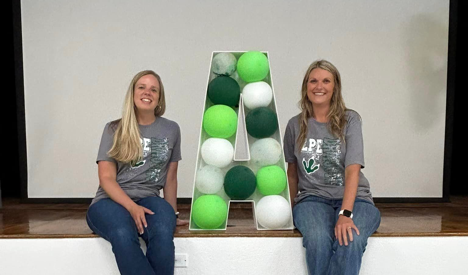 The principal and assistant principal sitting with the letter A filled with green balloons to show off their school grade for the year.