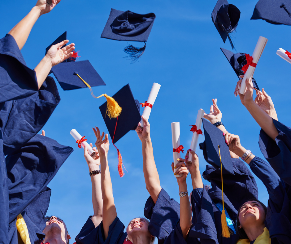 Graduates in blue gowns toss caps into the air with red tassels and hold diplomas against a blue sky.