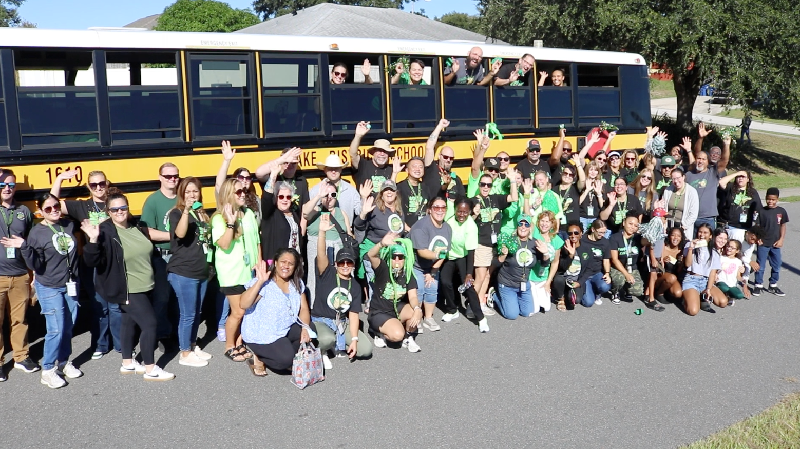 A group of people in green and black shirts posing for a photo in front of a yellow school bus.