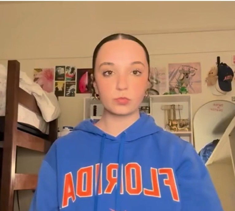 Person in a blue hoodie stands in a room with bunk beds and a mirror.