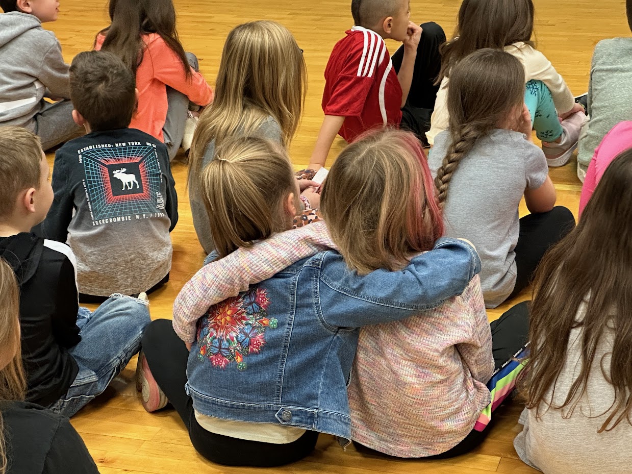 Two friends arms around necks, enjoying an assembly.