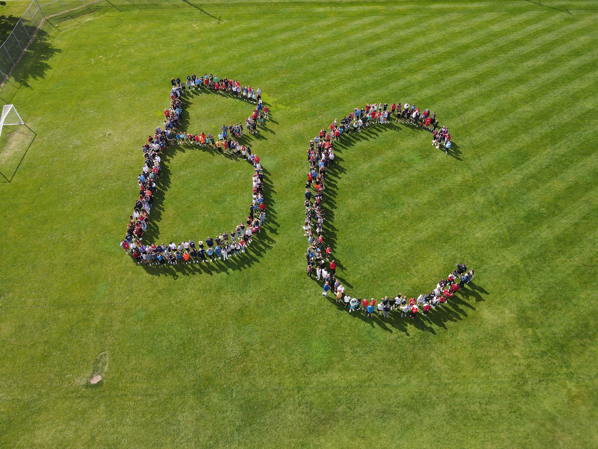 students and staff spelling B C on grass 