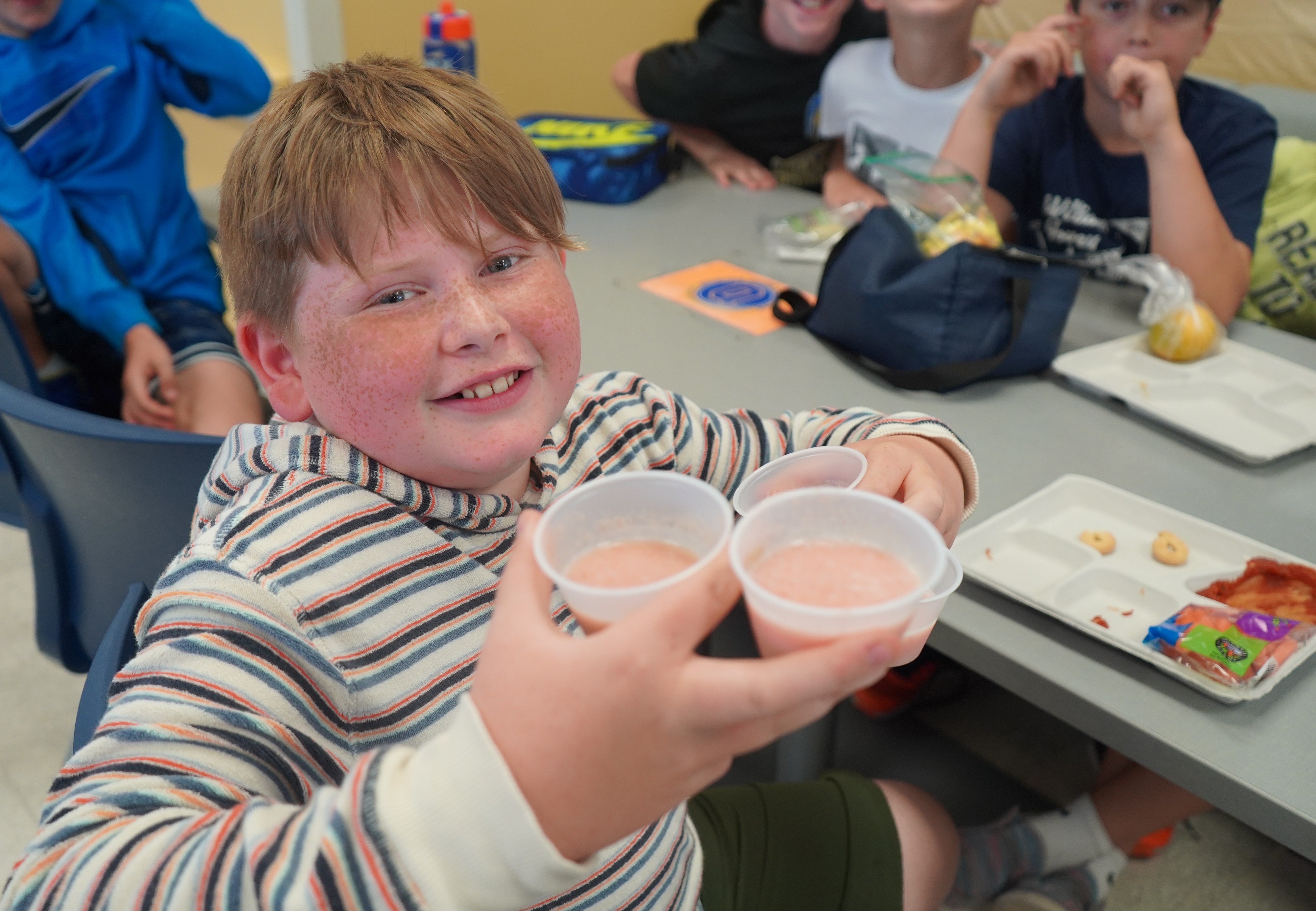 Boys holds three cups of smoothie.