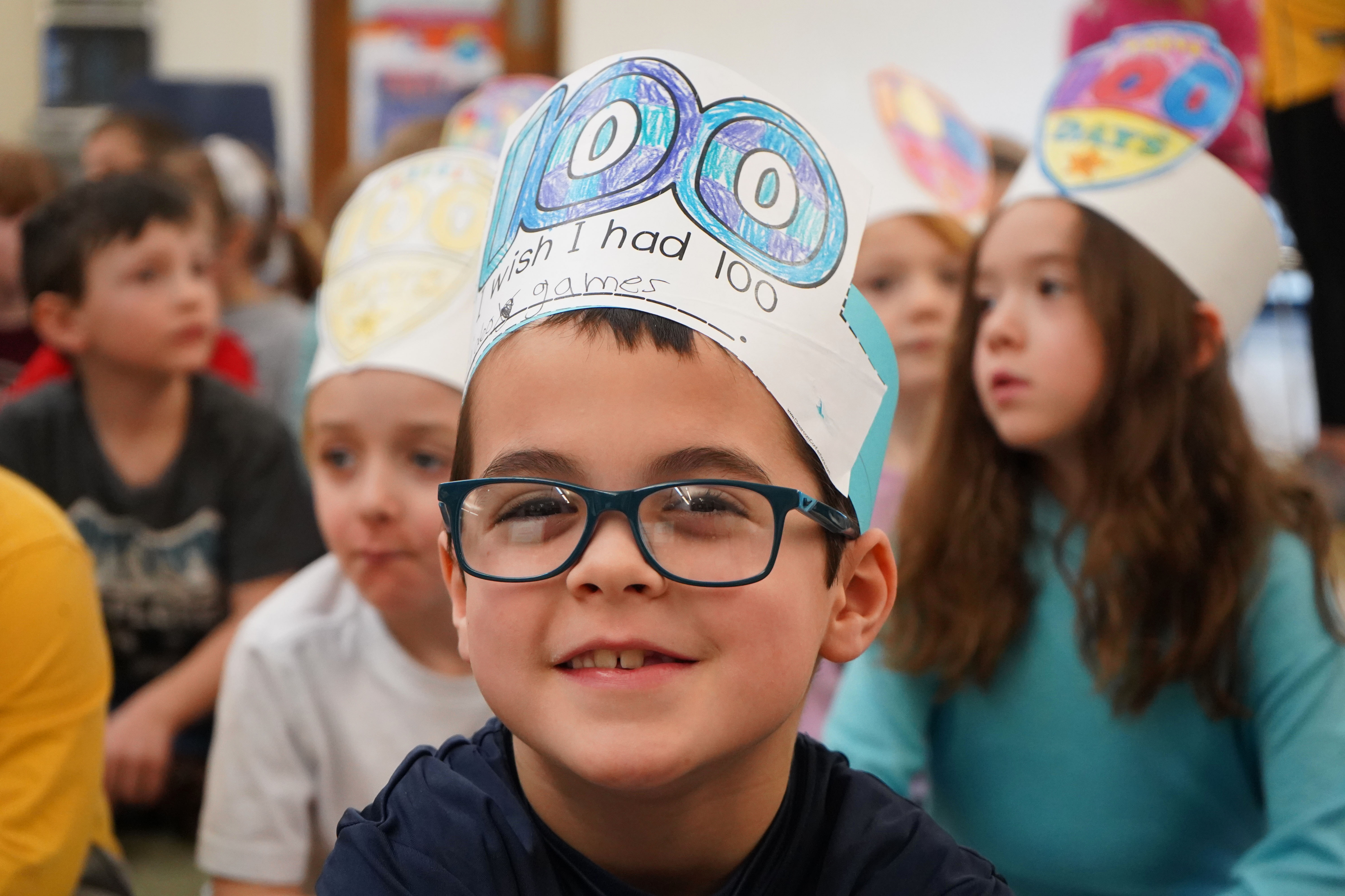 Young boy in glasses wears hat on 100th day of school.
