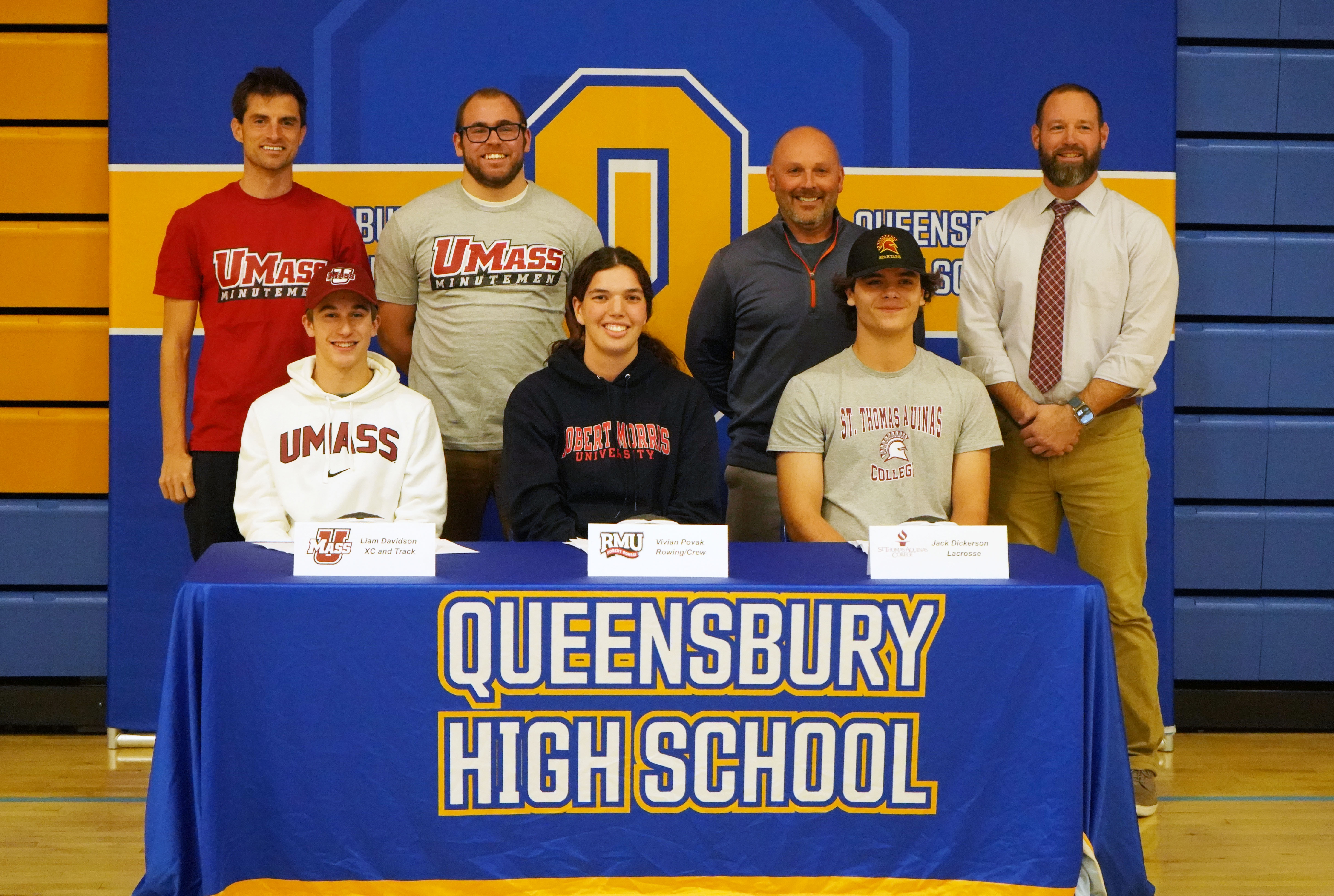 Three student-athletes sign letters of intent and pose for photo with coaches.