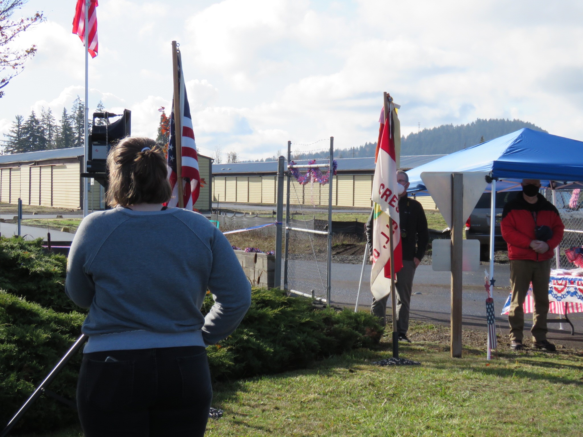Image of a young woman singing the national anthem in front of multiple American flags. 