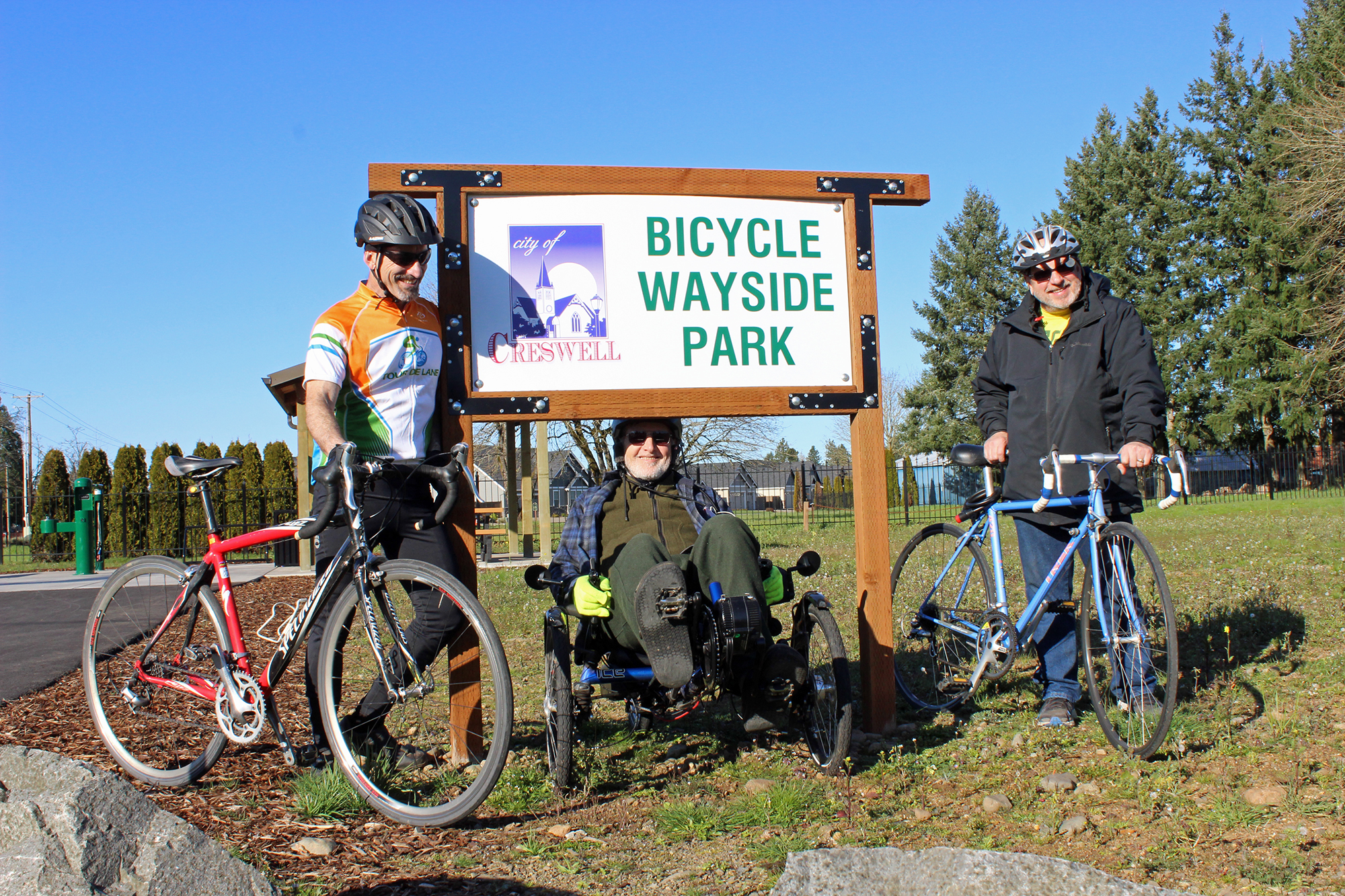 Image of three bicyclists in front of the Wayside Bicycle Park Sign