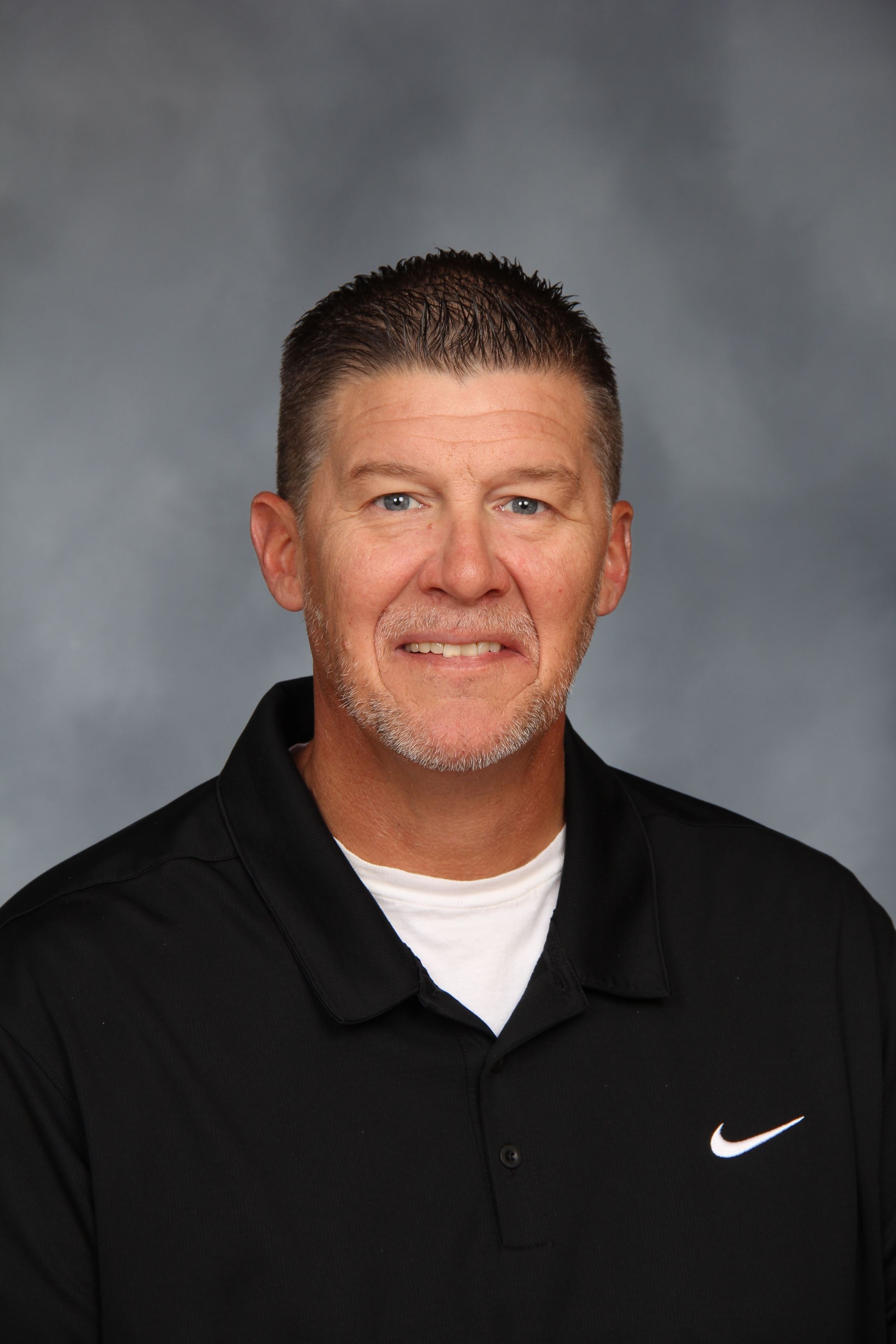 A man in a black polo shirt with the Nike logo on the left chest area smiles at the camera.