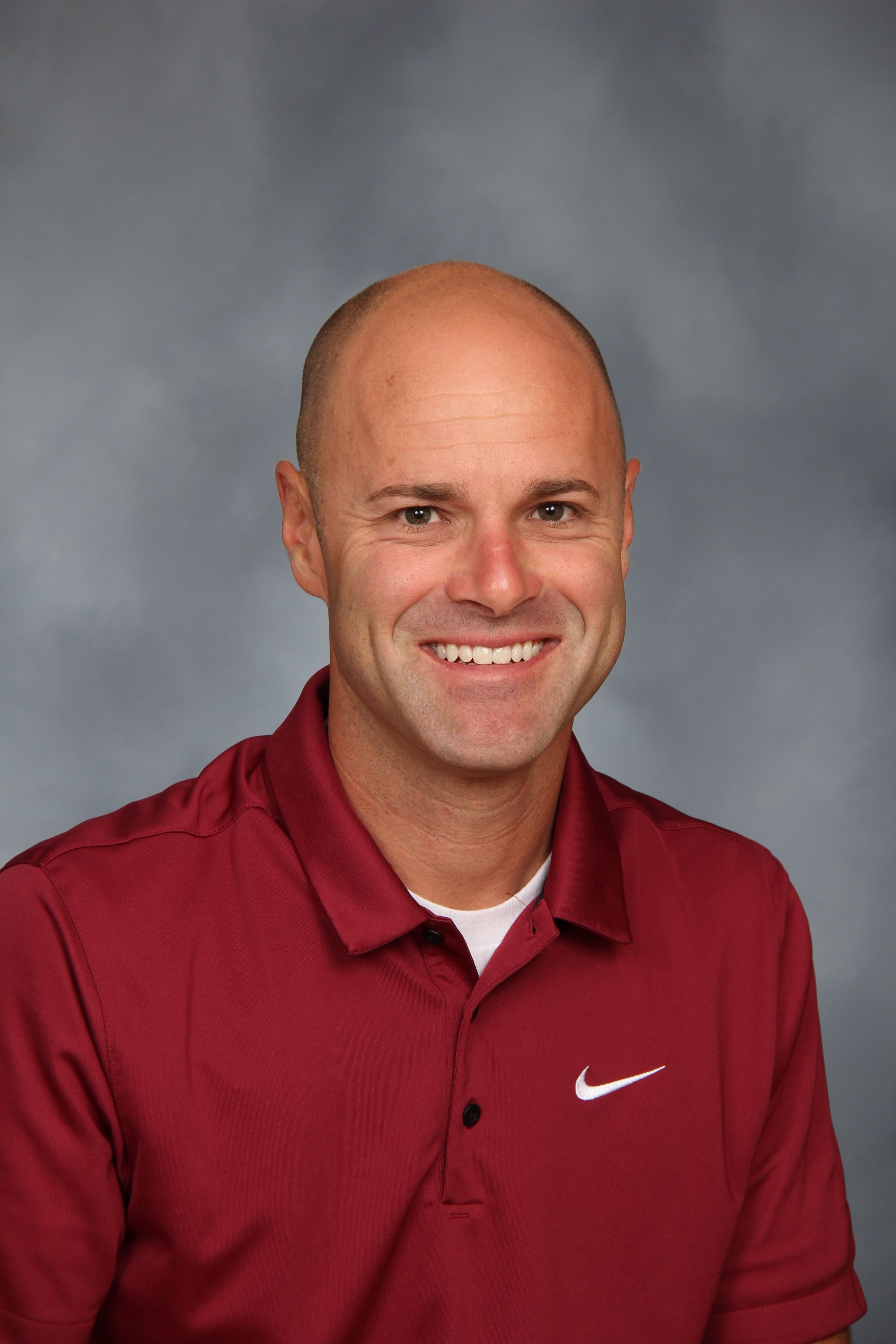 Man in a maroon polo shirt with a Nike logo on the left chest, smiling at the camera.