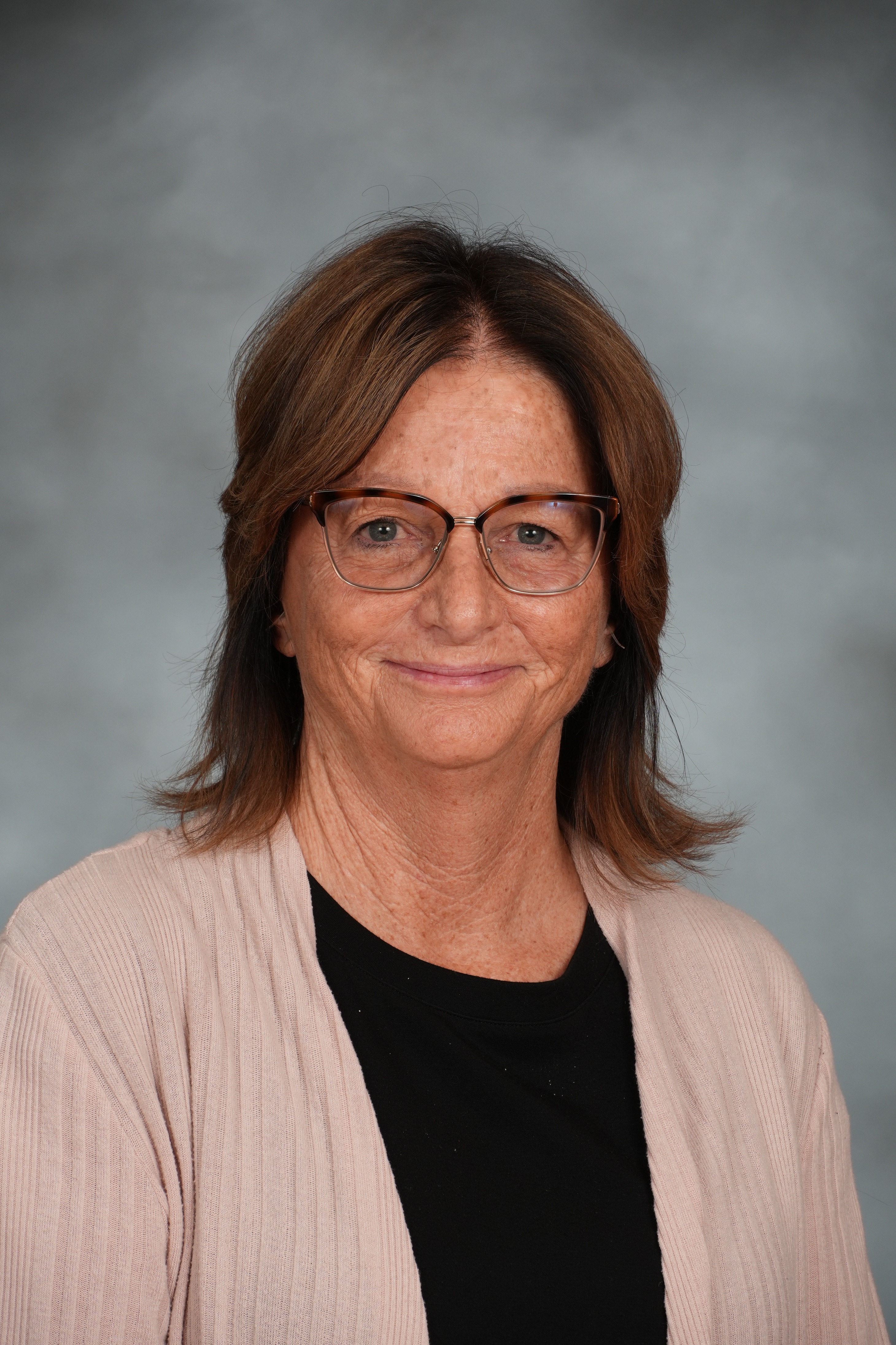 Woman with short hair, wearing glasses and a black top, under a light pink cardigan, smiling at the camera.