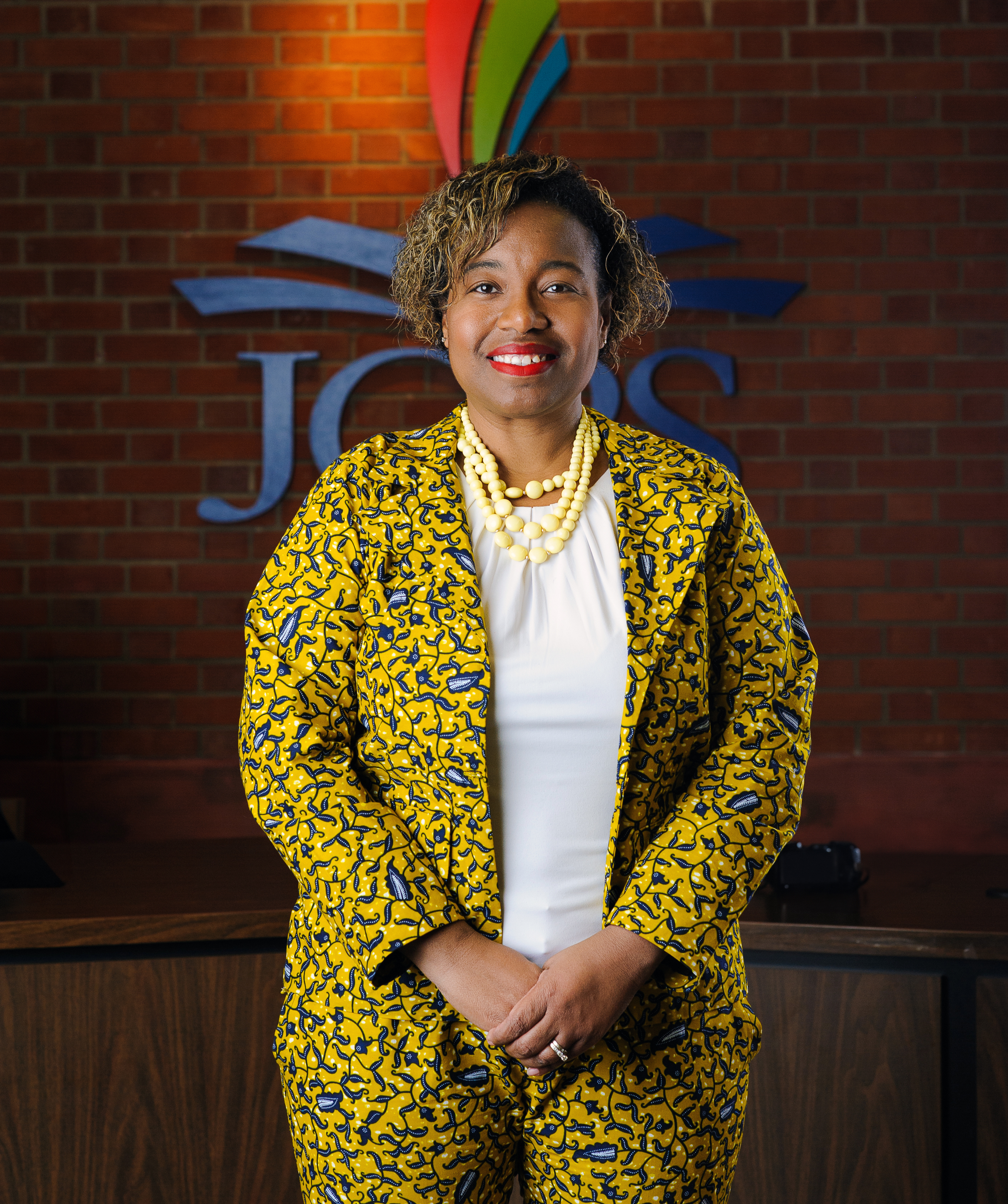 Photo of director.  It is an image of a black woman wearing a yellow suit with a white shirt.