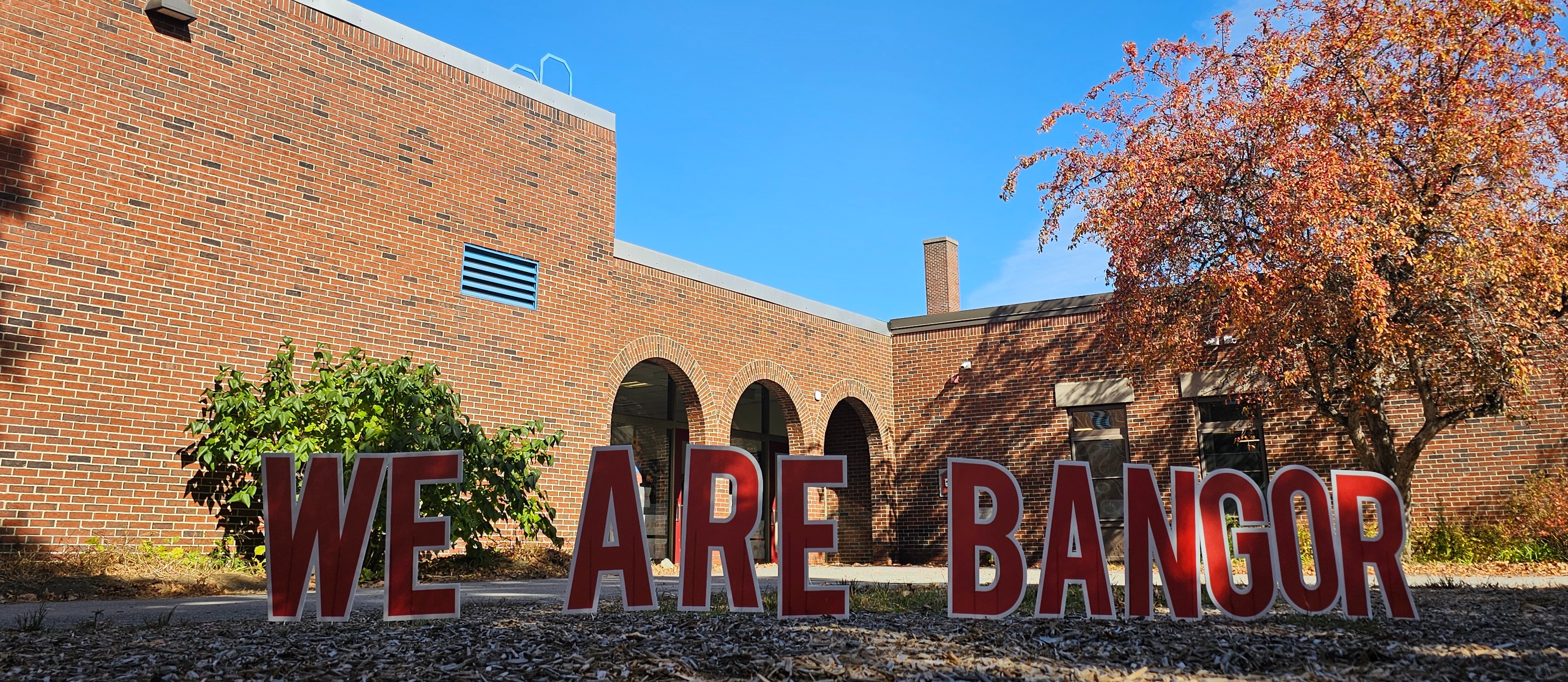 front of Abraham Lincoln School with the words, We Are Bangor in red letters with arches of the school in the back ground