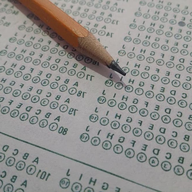 Scratchy pencil poised over a green and white paper exam, filled with bubbles, indicating answers have been selected.