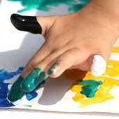 A child's hands wearing blue and green finger paint, creating an artful mess.