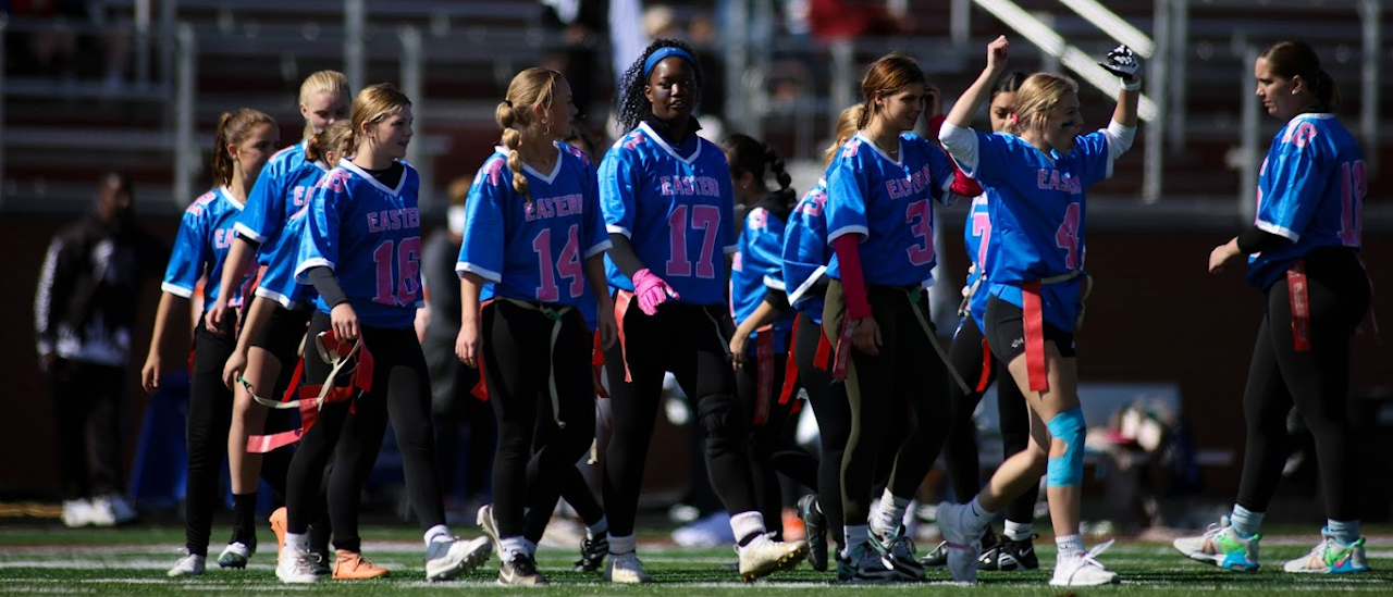 in blue and pink uniforms on a football field, standing together with smiles.