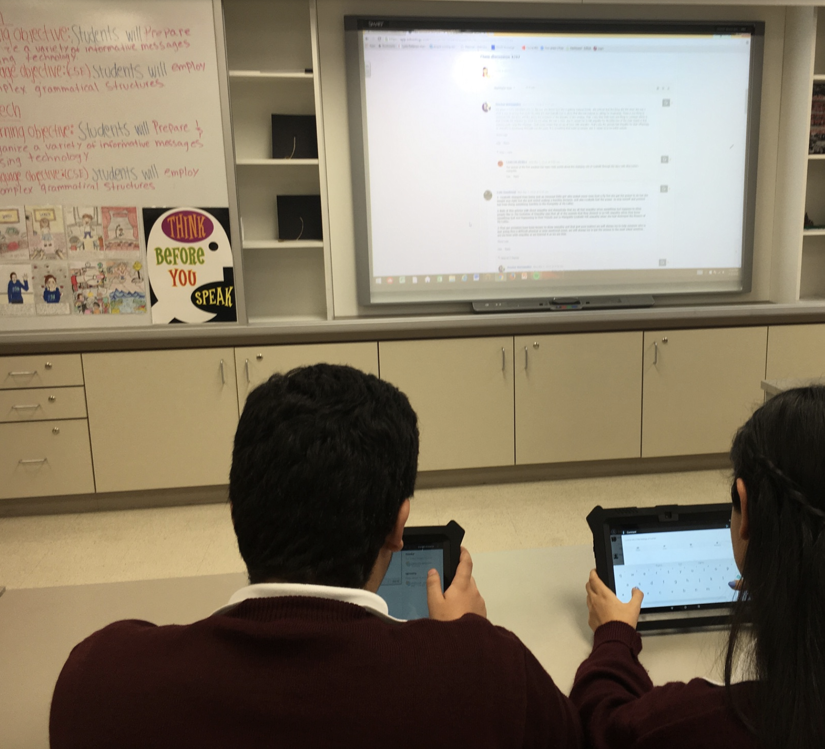 Boy and girl using a keyboard to interact with a smartboard in a classroom