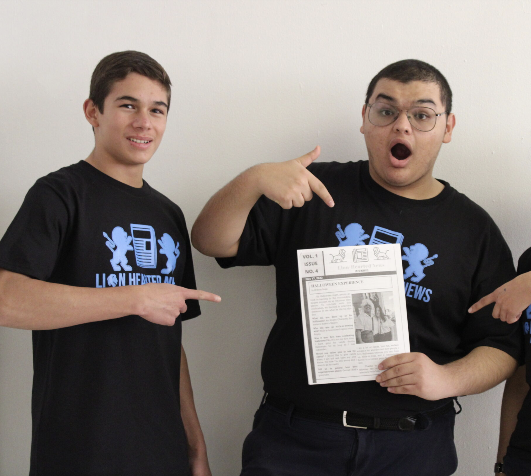 Two boys pointing to a newspaper created by students.