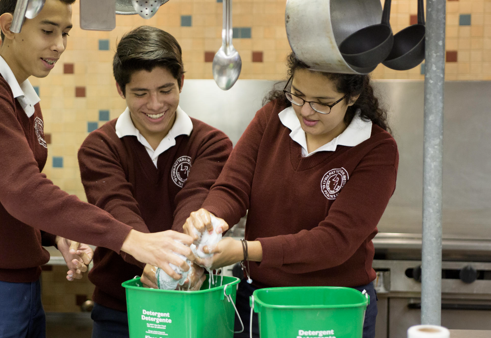 Three students squeezing a sponge in a bucket.