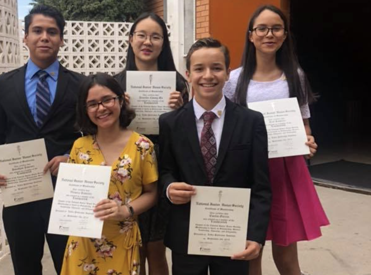 Students posing for the picture in a formal attire and holding some diplomas