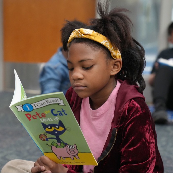 Student reading "Pete the Cat Saves Up".