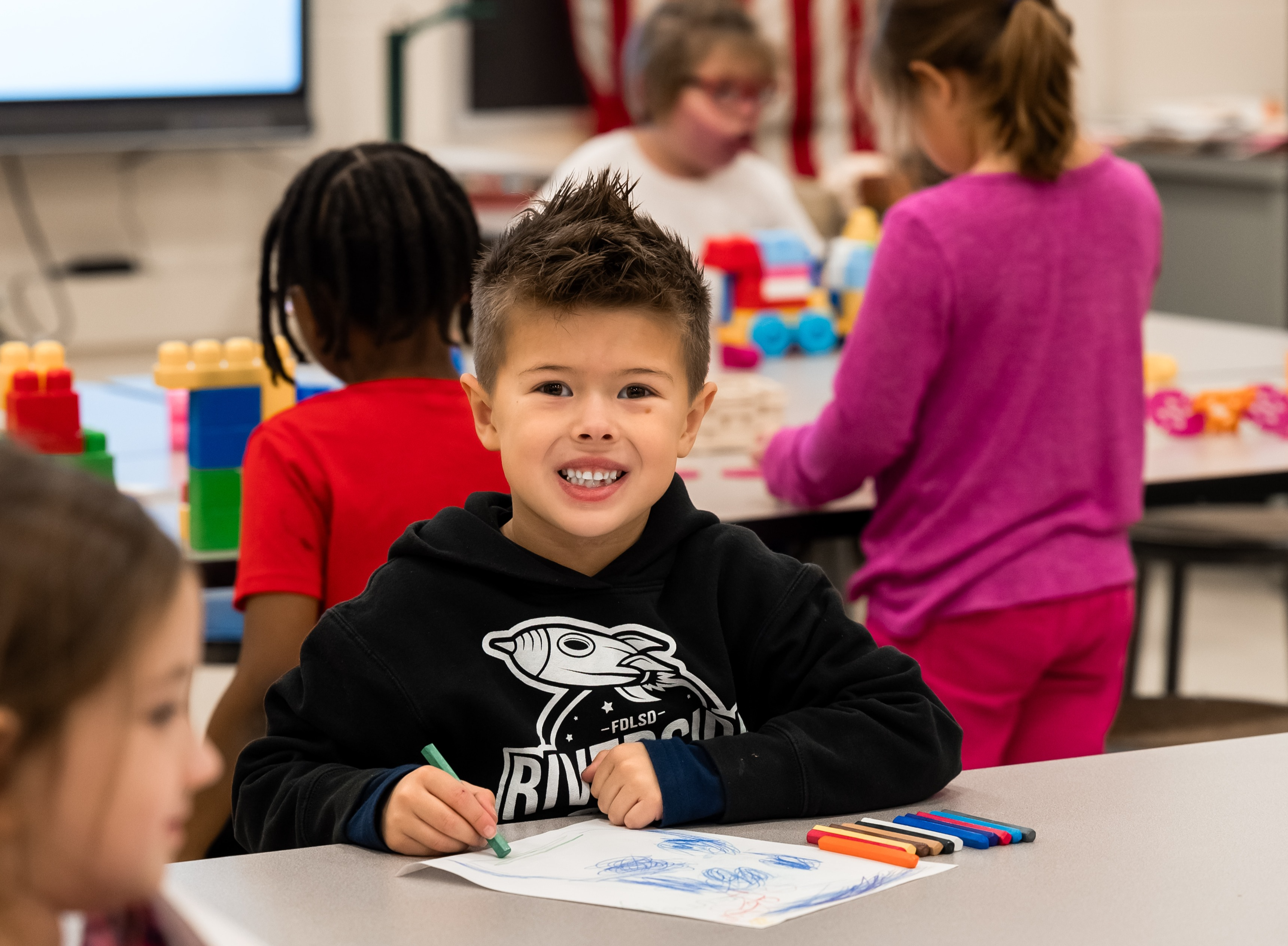 Darwin,First-Grader at Riverside Elementary School smiling at the camera while coloring with crayons in the classrom