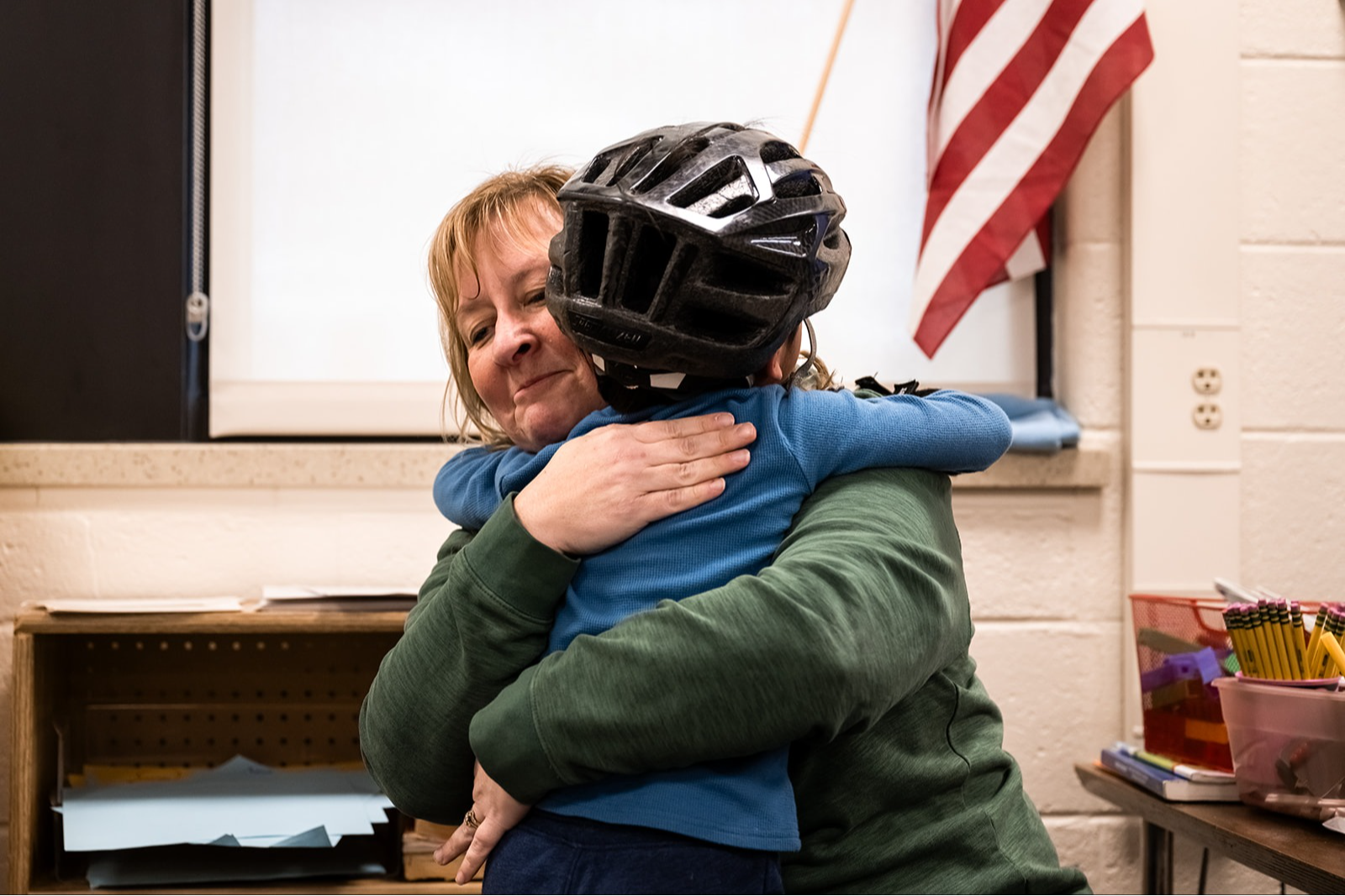 Kim Trent, Kindergarten Teacher at Evans Elementary School embracing a child wearing a helmet  in the classroom