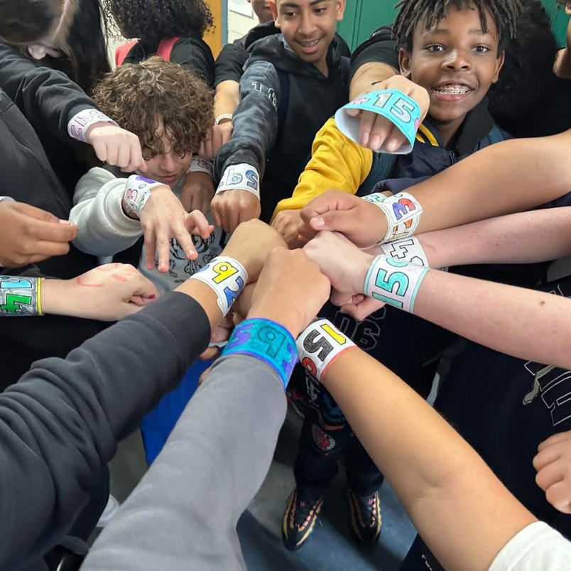 Kids put their hand in the middle of a student huddle
