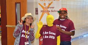 Three students posing together in a school hallway, one of them holding up their hand with three fingers to make the peace sign.