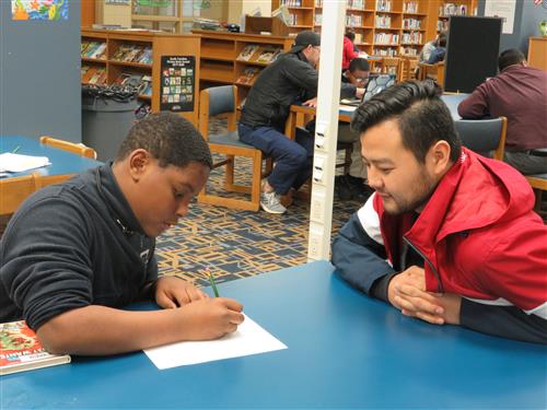 student writing and a teacher sitting in front of him