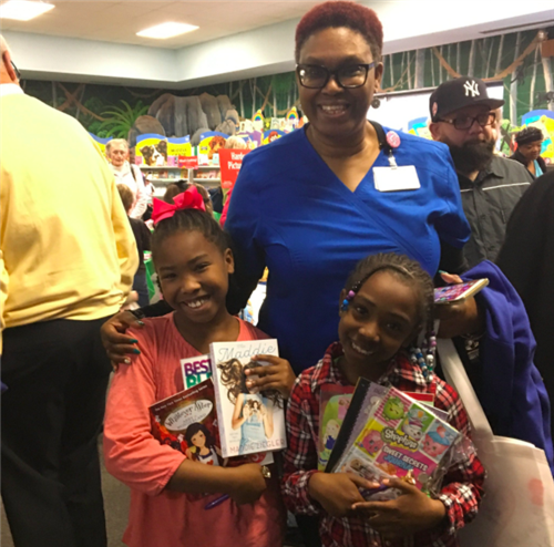 Picture of a teacher smiling with two children while they are holding books