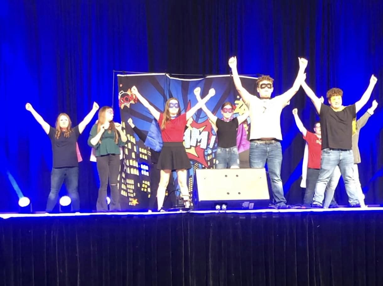 a blue lit stage with students dressed as super heros performing