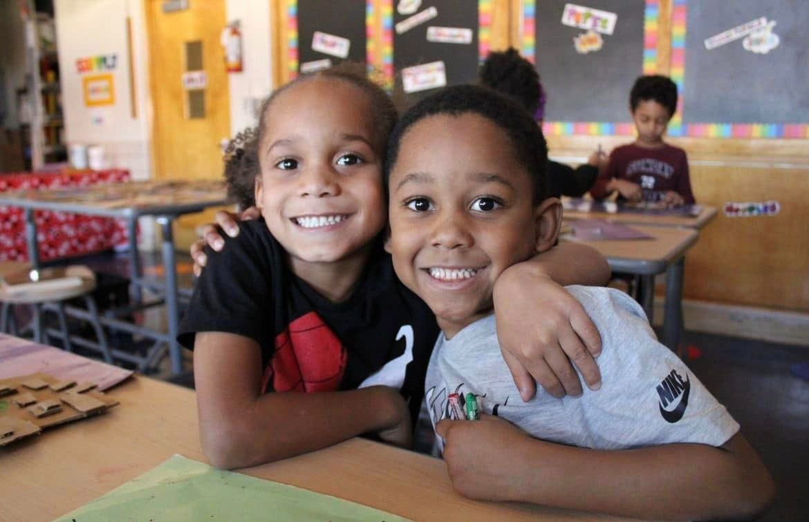 Students hugging in classroom at their desks