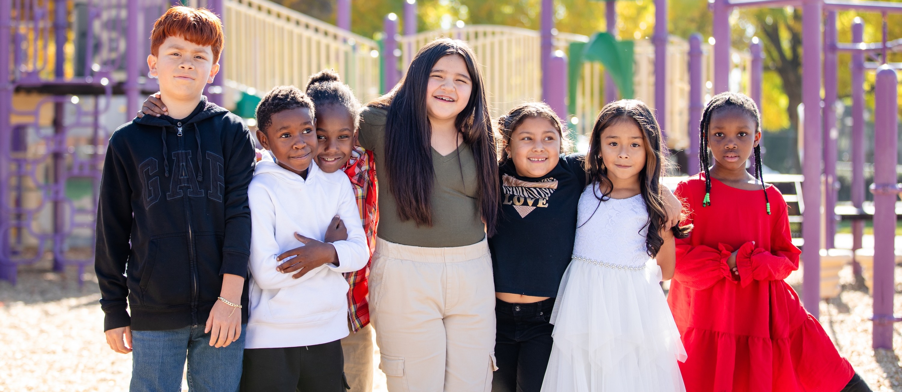 7 students with arms around each other posing on playground