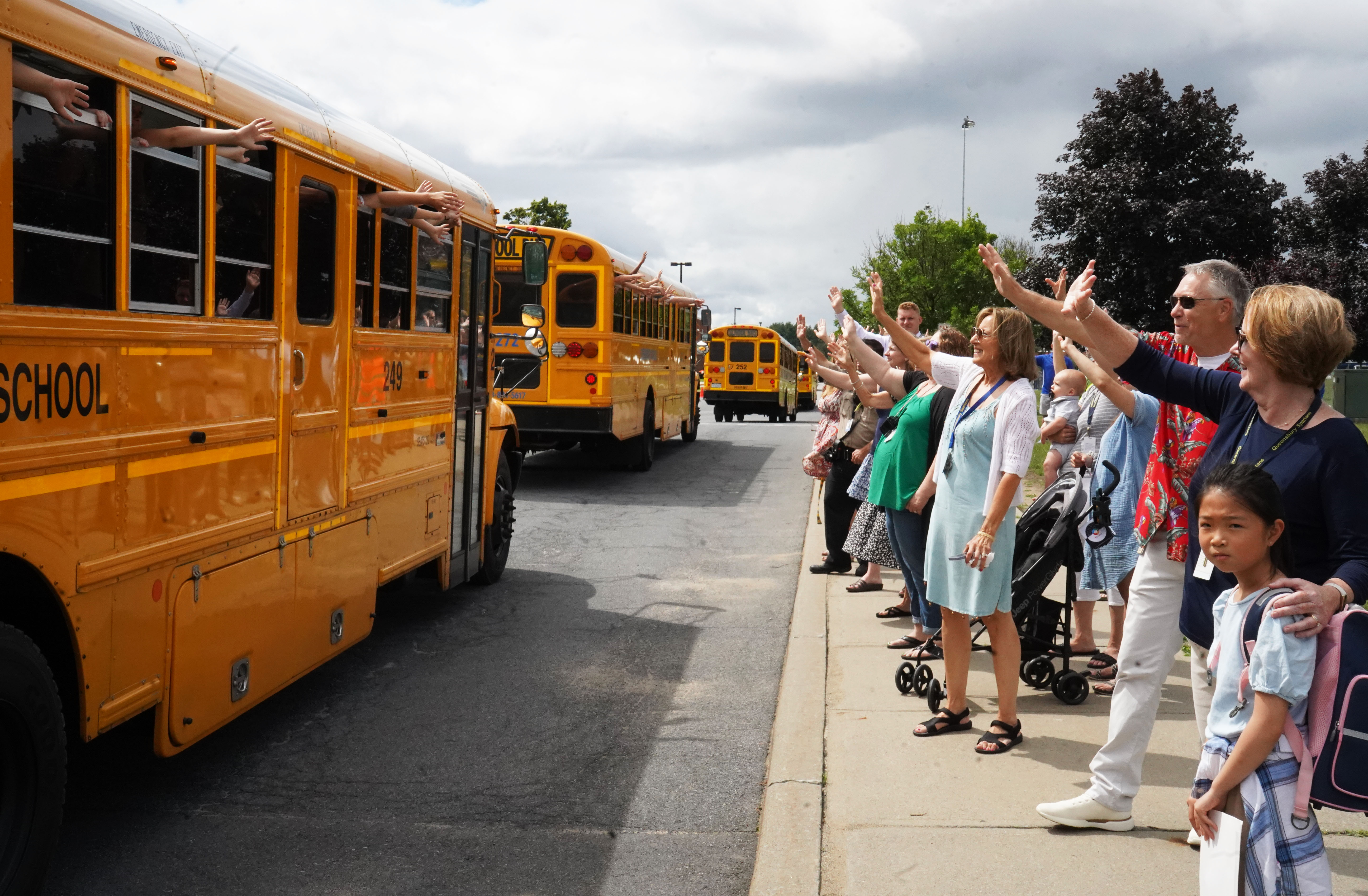 School staff and teachers wave goodbye to buses on the last day of school. 