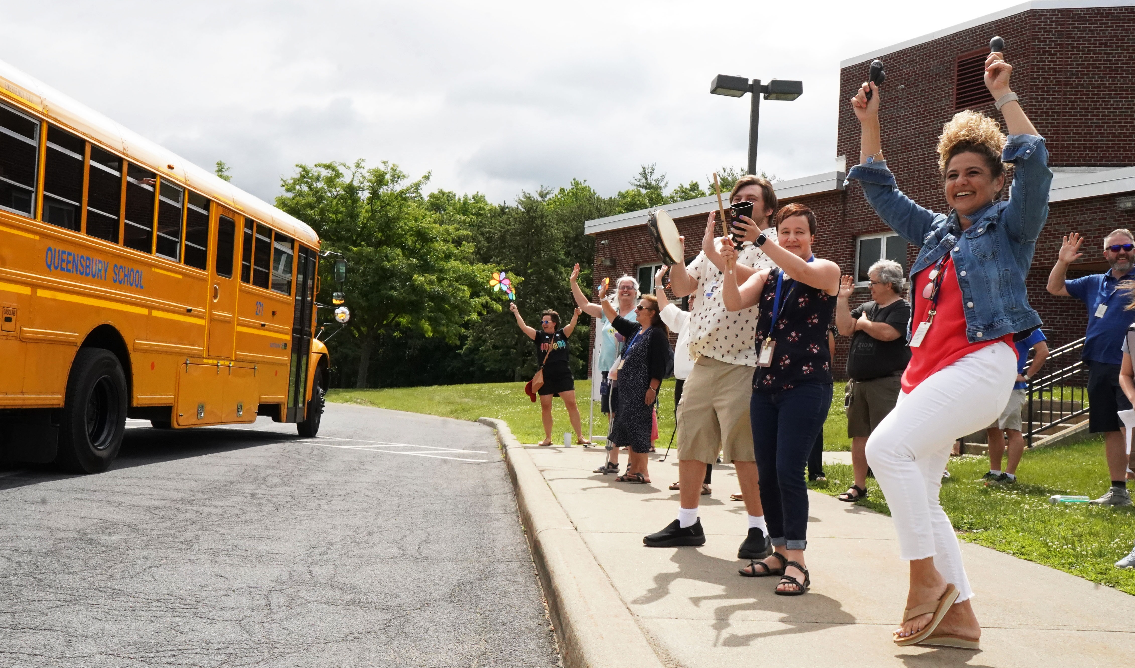 Teachers and staff wave to buses on the last day of school. 