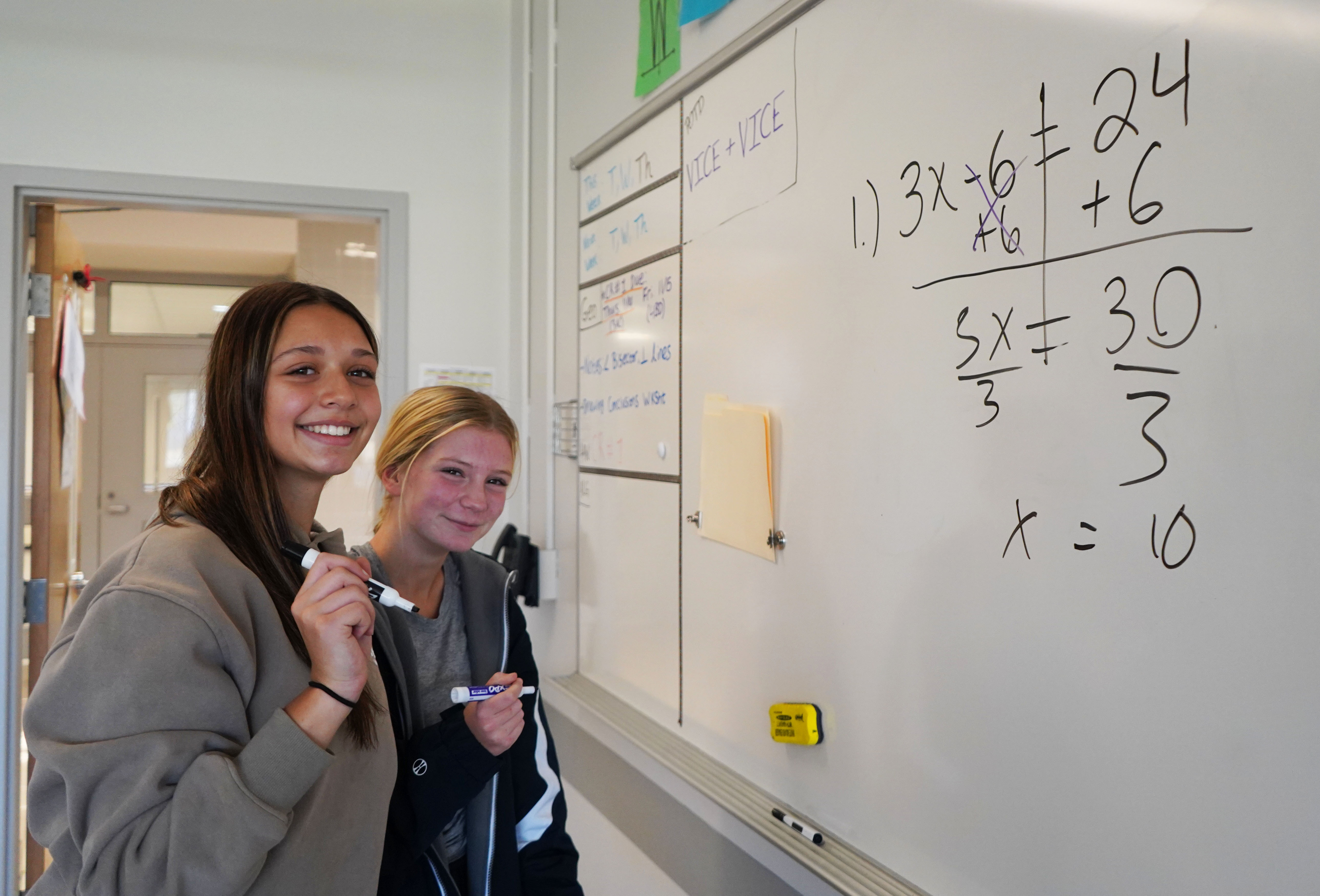 Two students do math at the white board. 